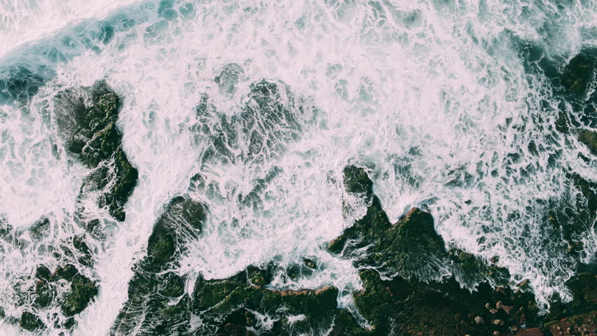 Abstract aerial view of ocean waves crashing on rocky shoreline