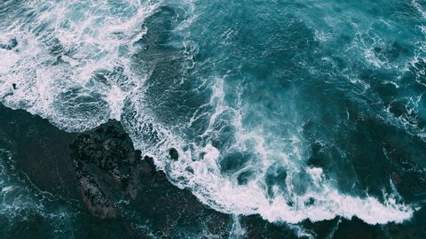 Abstract aerial view of ocean waves crashing on rocky shoreline