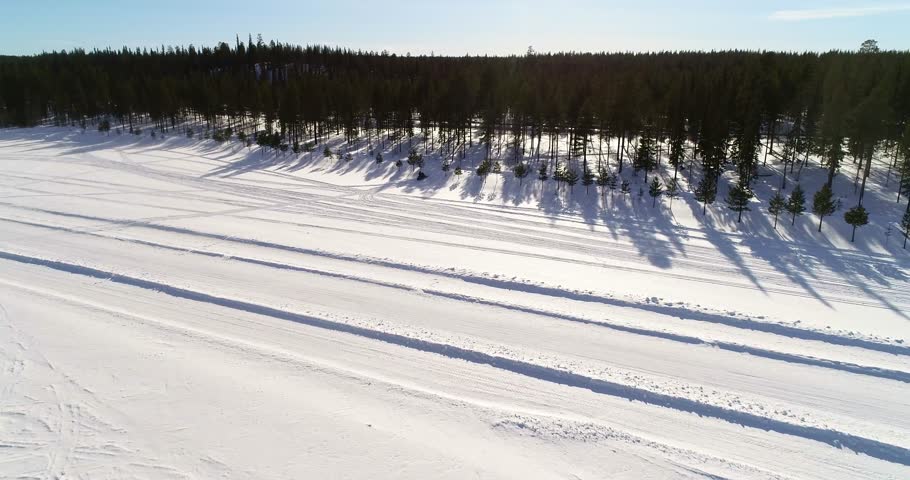 Snowmobile, C4k aerial view following a skidoo , driving through a snowy forest, near sallatunturi mountain fell, on a sunny winter day, in Salla, Lapland, Finland
