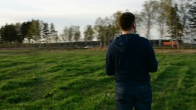 Young man controling drone in field at sunset.