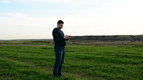 Young man controling drone in field at sunset.
