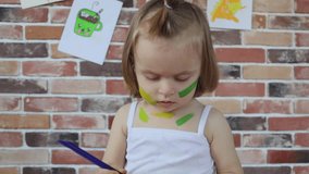 A little girl paints with paint and brush on face, slow motion video