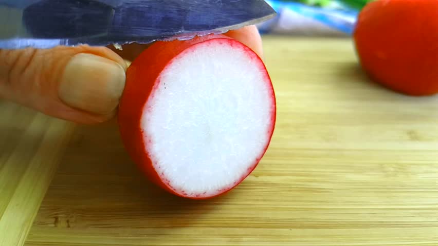 knife cuts radishes on a wooden board slow-motion shot