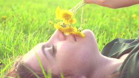 Beauty young woman lying on blooming field and smelling dandelion flowers. Beautiful happy girl enjoying nature outdoor. Female on the meadow, Pollen Allergy free concept. Slow motion   