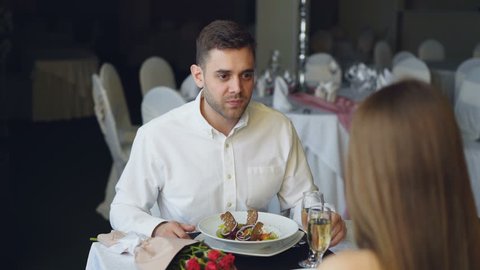 Young bearded man is arguing with his girlfriend while dining in restaurant then leaving. Lovers quarrel, negative emotions and relationship crisis concept.