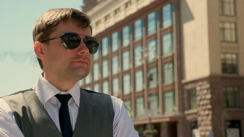Portrait of a man in sunglasses is standing on the street. He looks into the distance. The man takes off his sunglasses and corrects his hair.