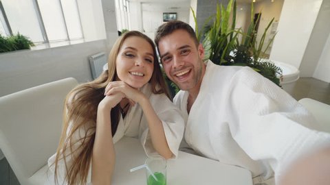 Point of view shot of attractive loving couple recording video while relaxing in day spa together. Young people are smiling, laughing and kissing looking at camera.