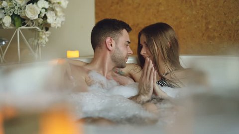 Newly married couple is relaxing in jacuzzi kissing, touching hands, talking and laughing. Romantic relationship, passionate honeymoon and wellness concept.