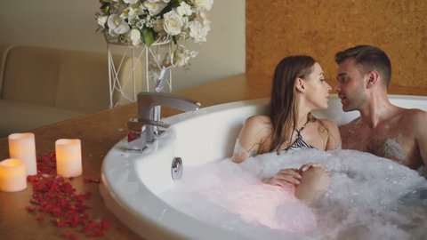 Adorable young couple is having fun and talking in bubble bath during romantic honeymoon. Romance, happy loving people and modern lifestyle concept.