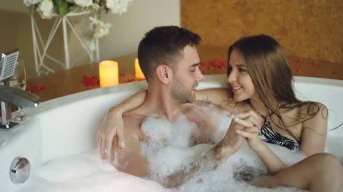 Young people in bathing suits are talking, hugging and touching hands in bathtub in spa salon. Romantic relationship, passion and wellness concept.