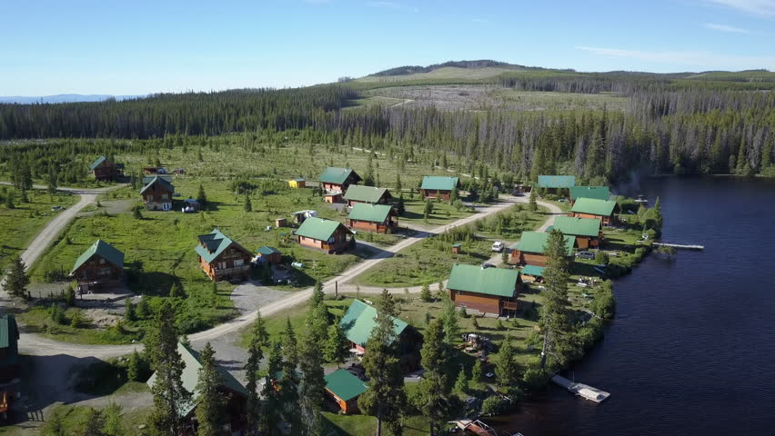 4k Aerial Drone Arc of Wooden Cabins with Green Roofs Beside a Lake in a Secluded Cleared Out Path of Trees in Forest in Canada