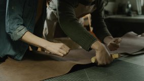 Man instructing co-worker on cutting leather in workshop / Provo, Utah, United States