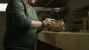 Slow motion tilt up to woman sanding wood block in workshop / Provo, Utah, United States
