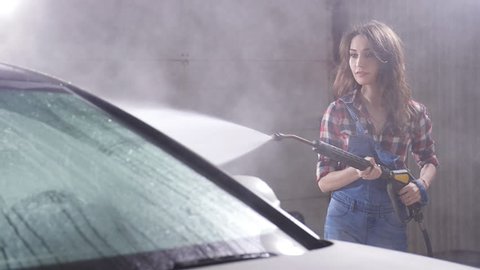 Young woman washes car with high pressure washing machine