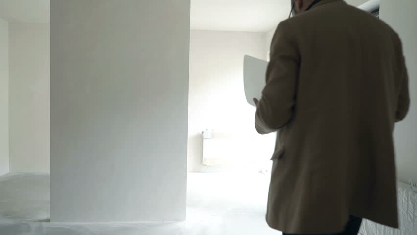 Young male architect checking documents and looking around at new home 

