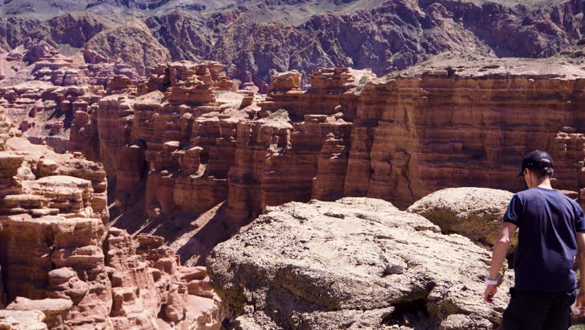 A young traveler stands on the edge of the cliff and raises his hands up enjoying the scenery