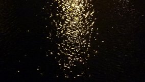 Stock footage shows a beam of light being reflected in flowing water at night.The water looks completely dark with the shiny reflection appearing like tiny golden stars spread on a dark background