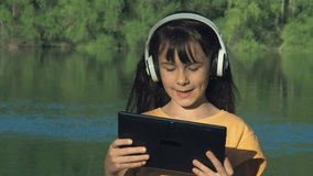 Video call. A child with a tablet on the nature. Girl with a tablet on the river bank.