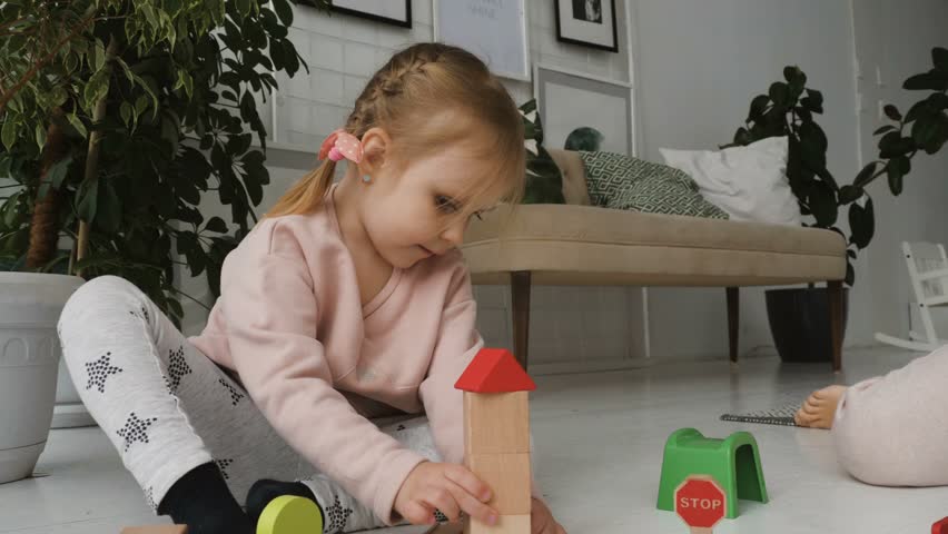 Close-up of little adorable girl is playing with wooden toy railroad while sitting on the floor in white living room