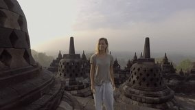 Slow motion video of travel young woman contemplating sunrise at Borobudur temple, Indonesia, smiling looking at camera