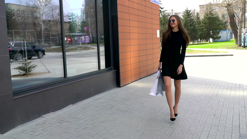 Young woman in little black dress spins around on the street. Beautiful young lady walking wish shopping bags after a shopping day. bag. Happy shopping woman, shopping girl in mall city, slow