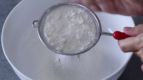 Hands sieving flour into a white mixing bowl	