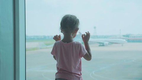 Little baby girl looks out of window at airport. 