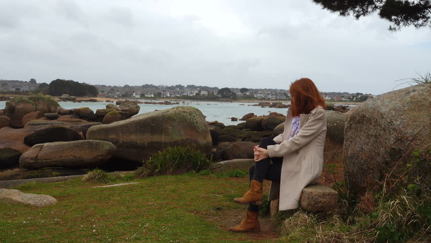 girl sitting on a bench and looking at the empty rocky shore at the low tide time, Brittany, France