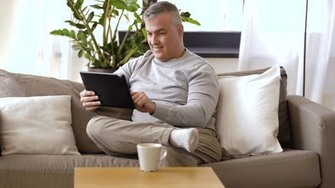 technology, people and lifestyle concept - man with tablet pc computer sitting on sofa at home