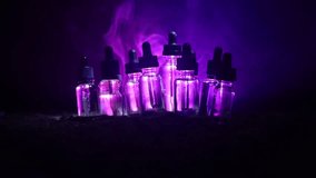 Slider shot. Vape (Electronic cigarettes) concept. Smoke clouds and vape liquid bottles on dark toned background. Light effects. Useful as background or vape advertisement. Selective focus