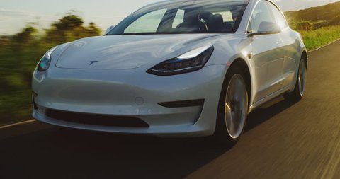 CALIFORNIA, USA - CIRCA APRIL 2018: The much anticipated Tesla Model 3 electric vehicle driving on country road at sunset.