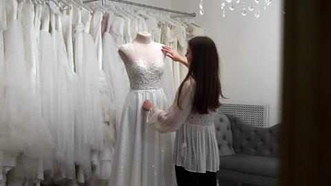 beautiful girl looking wedding dress in the cabin compared to other dresses. Preparing for the wedding. Buying a wedding dress. The seamstress inspects the finished custom made wedding dress.