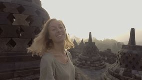 Slow motion video of travel young woman contemplating sunrise at Borobudur temple, Indonesia, smiling looking at camera