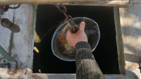 Man drops chain with bucket into rustic well to draw water.