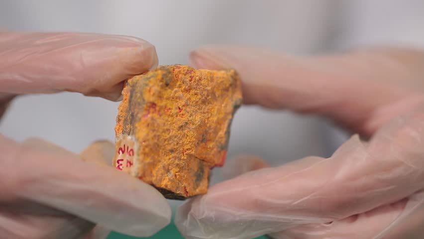 Female hands in white gloves holding stone mineral. Macro, orange rough stone. Hands holds amber. Semi-precious mineral in hand. Scientist studying the material close-up