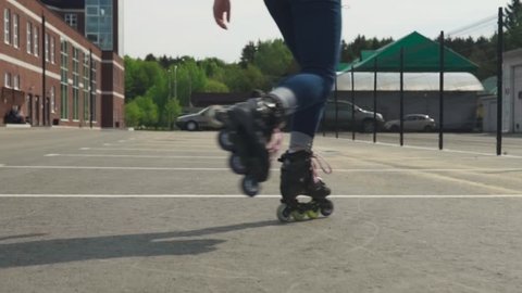 Young woman rides on roller skates and whirl on asphalt road in city, slow motion, steadicam shot