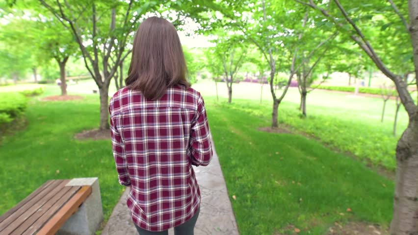 Young pretty girl walking on path in the park and drinking a cup of coffee