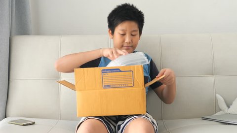 Asian boy unboxing and opens the bubble bag from the online store. He is surprised and happy to receive a surprise. Slow Motion.