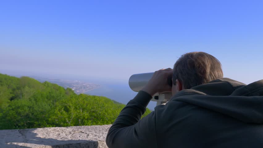male traveler looking through a telescope on top of a mountain. 4k, slow motion