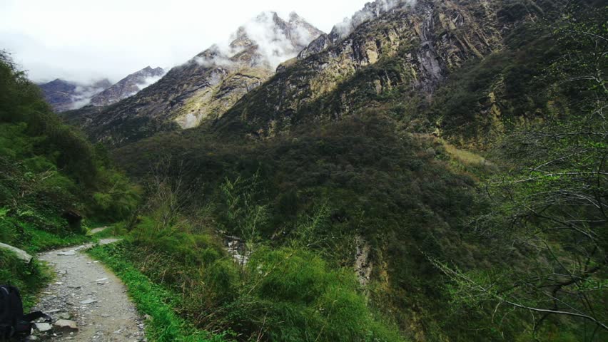 Narrow path with steep cliff among high mountains and green forest. Landscape mountain valley and peaks in misty haze