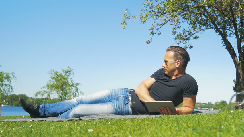 Weekend in the city - a man relaxes on the grass in the park and reads a book