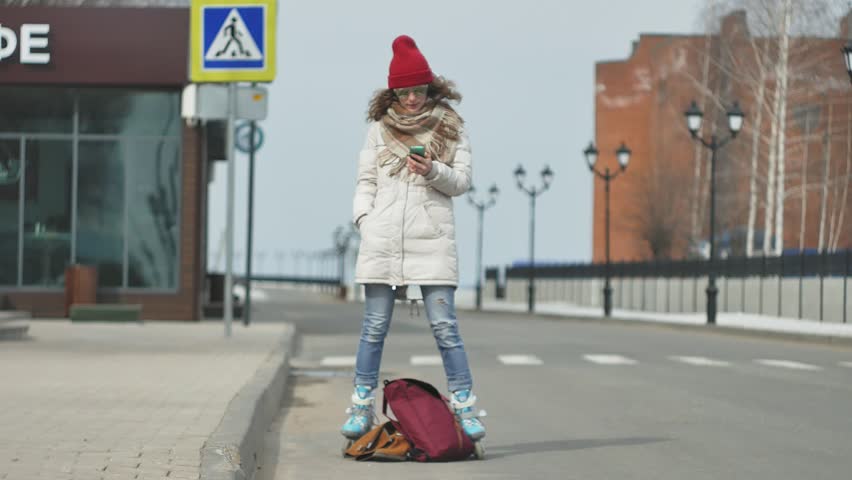 Young beautiful woman in a red hat, wearing sporty warm clothes and rollers, riding on the road on the coast 4k