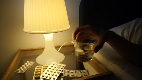 A lot of medications pills tablets on bedside table. Sick man sleep in bed, switch on night lamp, take glass of water, drink, turn off light. Self-medication concept. Filmed 4K Sony a6300.
