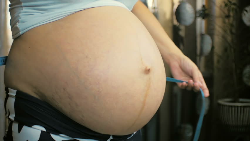 Close-up of a young pregnant girl measures the volume of her belly indoors.