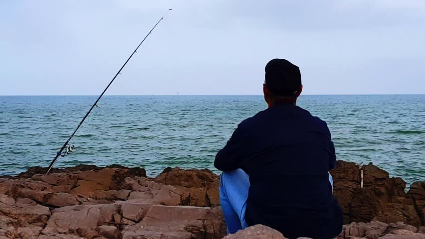 A man sits on a rock and looks out to sea.