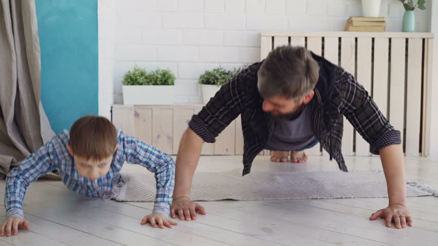 Active handsome father and his joyful son are exercising doing press-up together at home on wooden floor. Happy family, sport and sporty lifestyle concept.