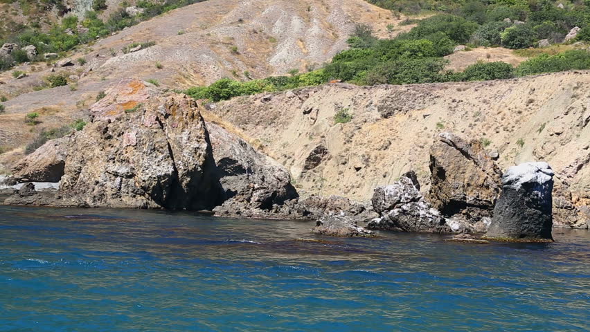 The fragments of the rock are in the water off the coast. View from the sea. The camera moves to the right to the left.