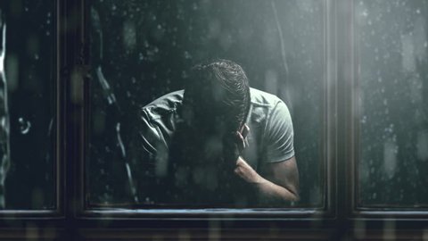 Sad man holding head with hand, sitting in dark room. rainy day