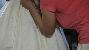 Close-up of woman hand buttoning the wedding dress. Bridesmaid helps zip up wedding dress.
