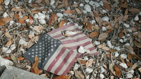 Grungy red, white, and blue American flag lays on the ground covered in dirt. Neglected United States flag is a symbol of the failing values of America, deportation, desecration and anti-Americanism.
